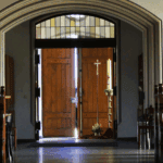 Kircheninnere mit offenem Holztür, Kerze und Kreuz, einladend und spirituell.