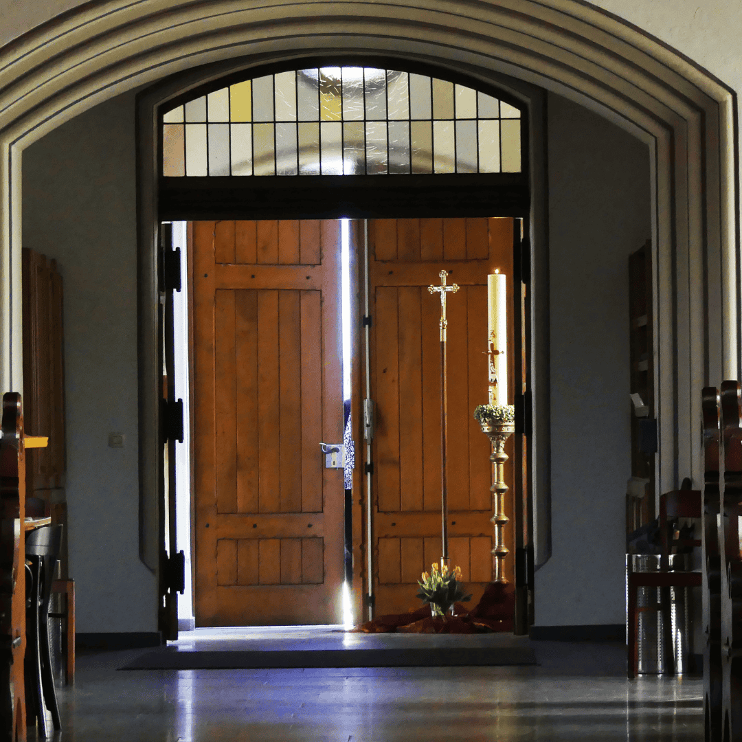 Kircheninnere mit offenem Holztür, Kerze und Kreuz, einladend und spirituell.