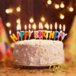 Geburtstagstorte mit brennenden Kerzen, die Happy Birthday buchstabieren, umgeben von Lichtern und Dekorationen.