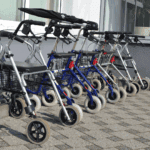 Mehrere Rollatoren nebeneinander auf einem Gehweg vor einem Gebäude geparkt.
