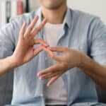 Mann in blauer Hemd zeigt eine Geste, die Gebärdensprache oder Kommunikation symbolisieren könnte.