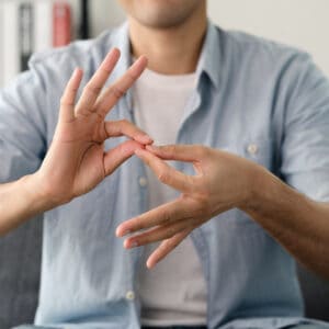 Mann in blauer Hemd zeigt eine Geste, die Gebärdensprache oder Kommunikation symbolisieren könnte.