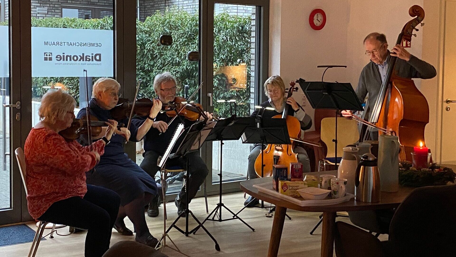 Älteres Kammermusikensemble spielt im Gemeinschaftsraum, mit Geige, Cello und Kontrabass.