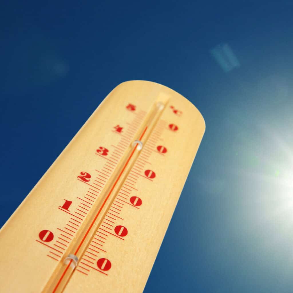 Thermometer in der Sonne zeigt hohe Temperatur an; blauer Himmel im Hintergrund, Sommerhitze Konzept.