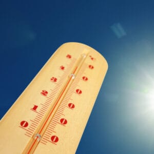 Thermometer in der Sonne zeigt hohe Temperatur an; blauer Himmel im Hintergrund, Sommerhitze Konzept.