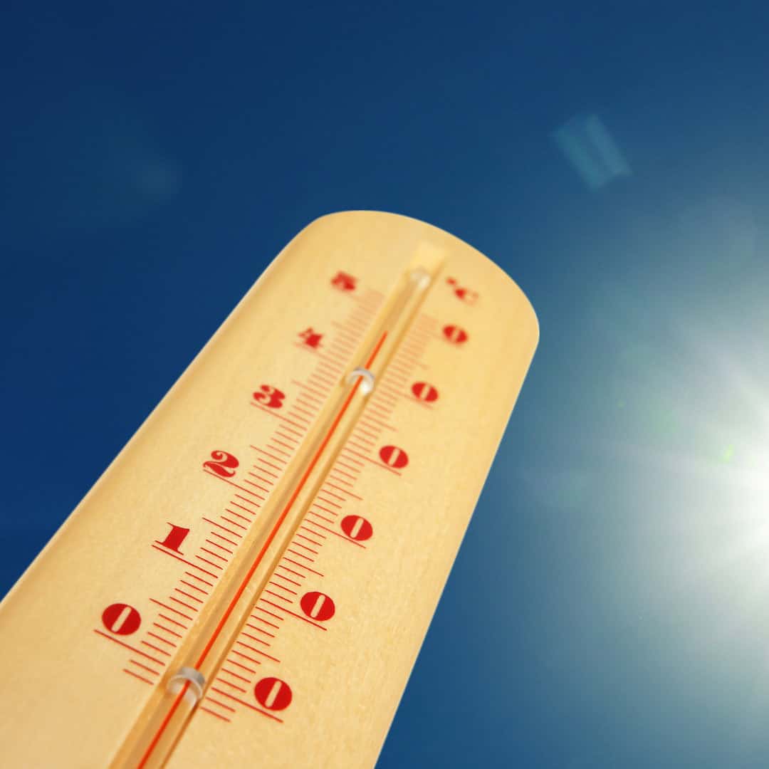 Thermometer in der Sonne zeigt hohe Temperatur an; blauer Himmel im Hintergrund, Sommerhitze Konzept.