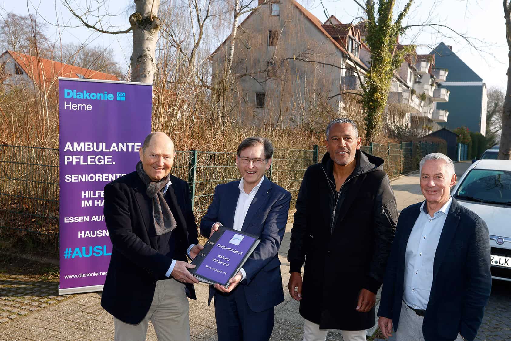 Gruppe bei Übergabe einer Bauunterlage für Diakonie-Projekt in Herne vor Plakat für ambulante Pflege.